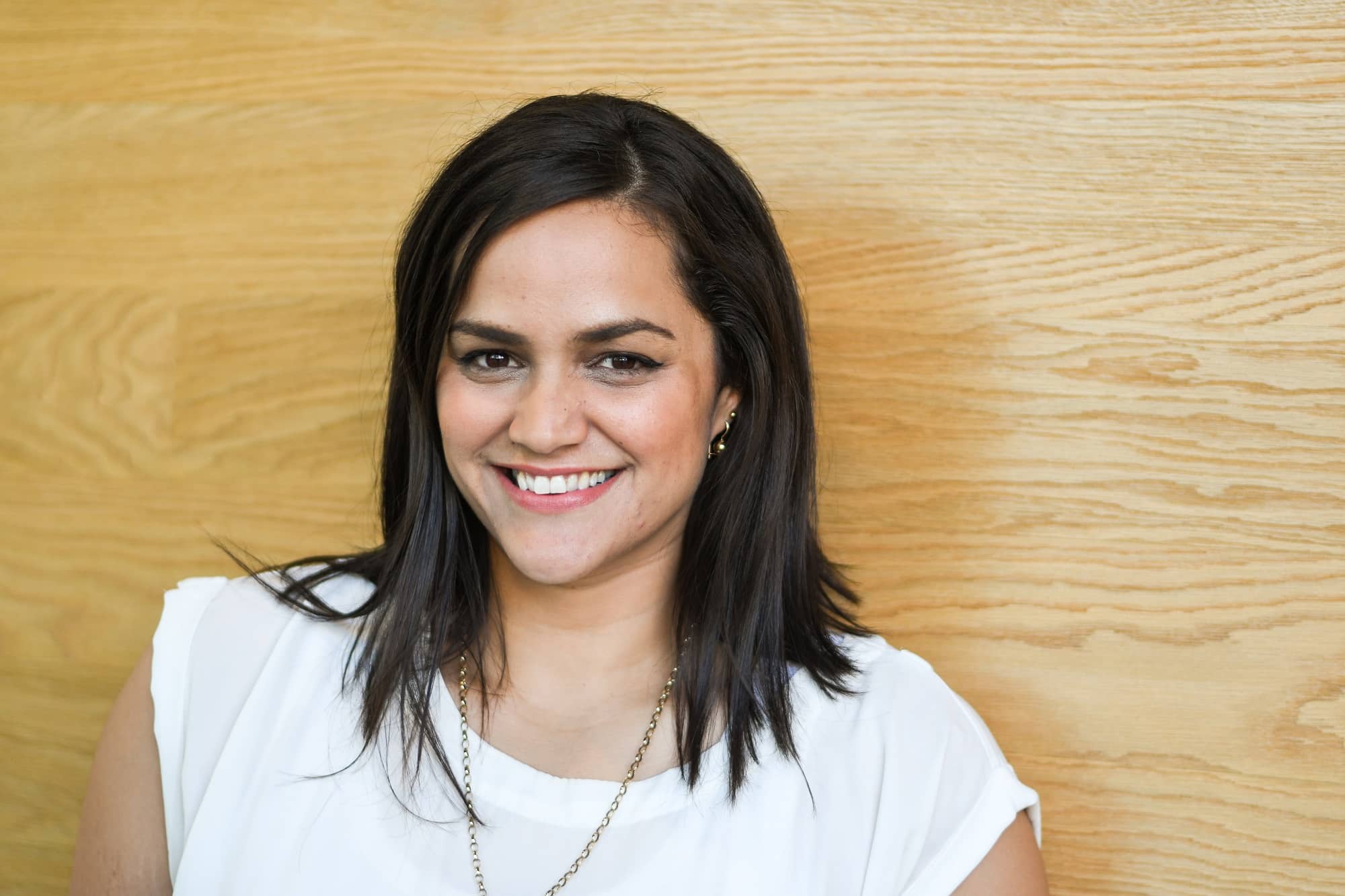 Happy, young, Maori female wIth shoulder length dstk haIr in busIness attIre on her own and against a wooden background