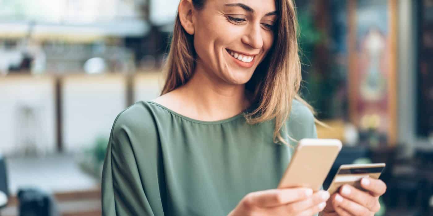 Young woman shopping online in cafe using smartphone and credit card