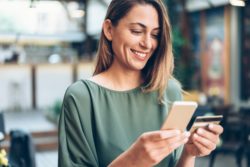 Young woman shopping online in cafe using smartphone and credit card