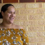 Portrait of a young Pacific Islander woman, standing in front of her home.