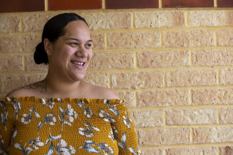 Portrait of a young Pacific Islander woman, standing in front of her home.