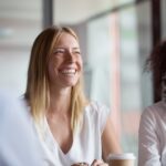 Happy young businesswoman coach mentor leader laughing at funny joke at group business meeting, joyful smiling millennial lady having fun with diverse corporate team people engaged in talking at work