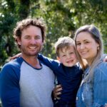 Father, Mother and young son together outdoors in sunlight in park wearing casual clothing - looking at camera