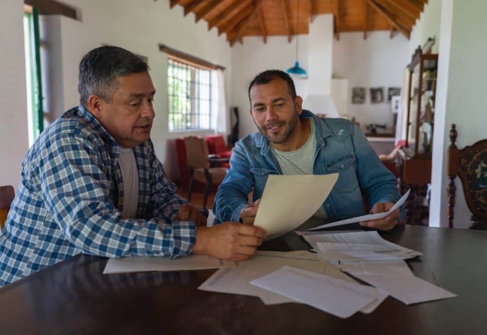 Latin American business owner talking to the overseer of a coffee farm and showing them their financial state on a laptop computer