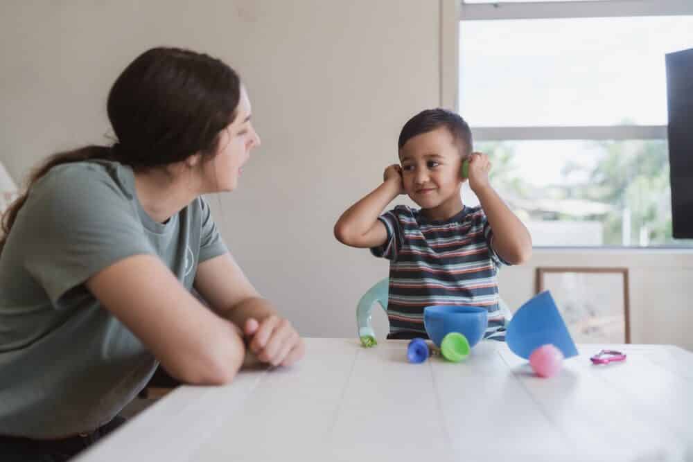 Kid playing with toys while mother sitting along him at home.