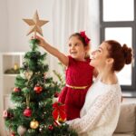 family, winter holidays and people concept - happy mother and little daughter decorating christmas tree at home