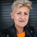 Front view portrait of senior woman standing against black backround, looking at camera.