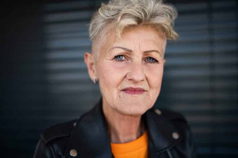 Front view portrait of senior woman standing against black backround, looking at camera.