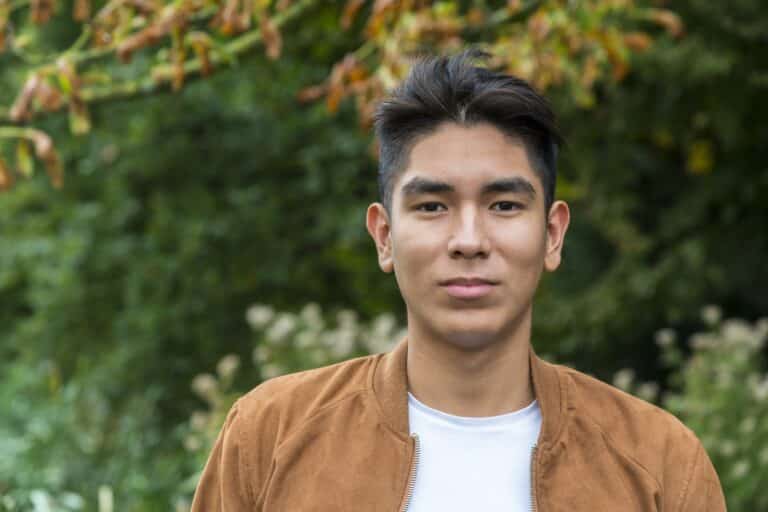 Portrait of a smiling Latin American young man with a brown suede jacket, shot outside