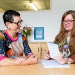 Two women at a table looking at a piece of paper smiling