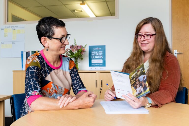 Two women at a table looking at a piece of paper smiling
