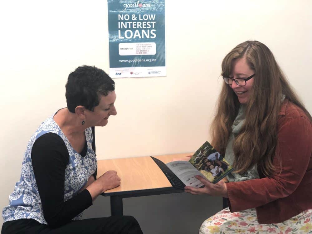 Two women sat at a desk looking at a piece of paper happily