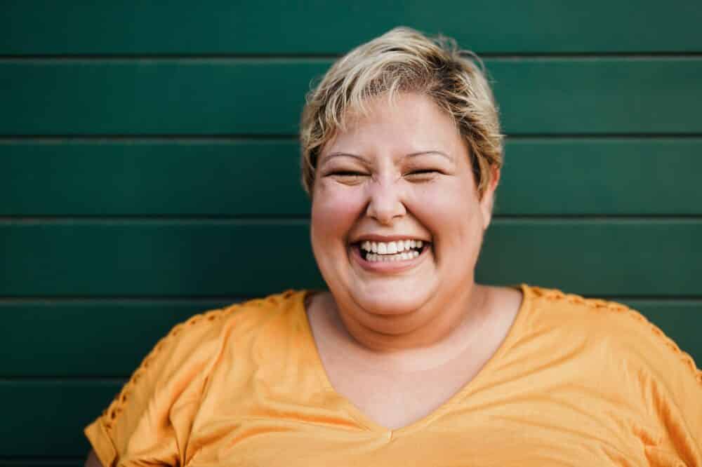 Portrait of woman smiling on camera outdoors with green background - Focus on face