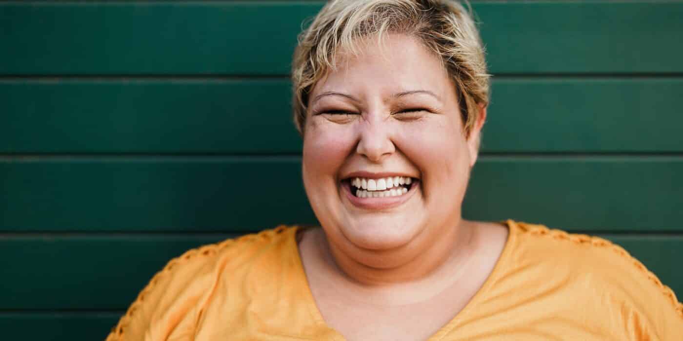 Portrait of woman smiling on camera outdoors with green background - Focus on face