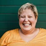 Portrait of woman smiling on camera outdoors with green background - Focus on face