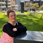 Hayley Tinning sat outside smiling on bench in sun