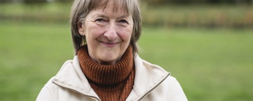 Portait of a senior woman standing in a field while at a farm in Autumn, smiling while looking at the camera.